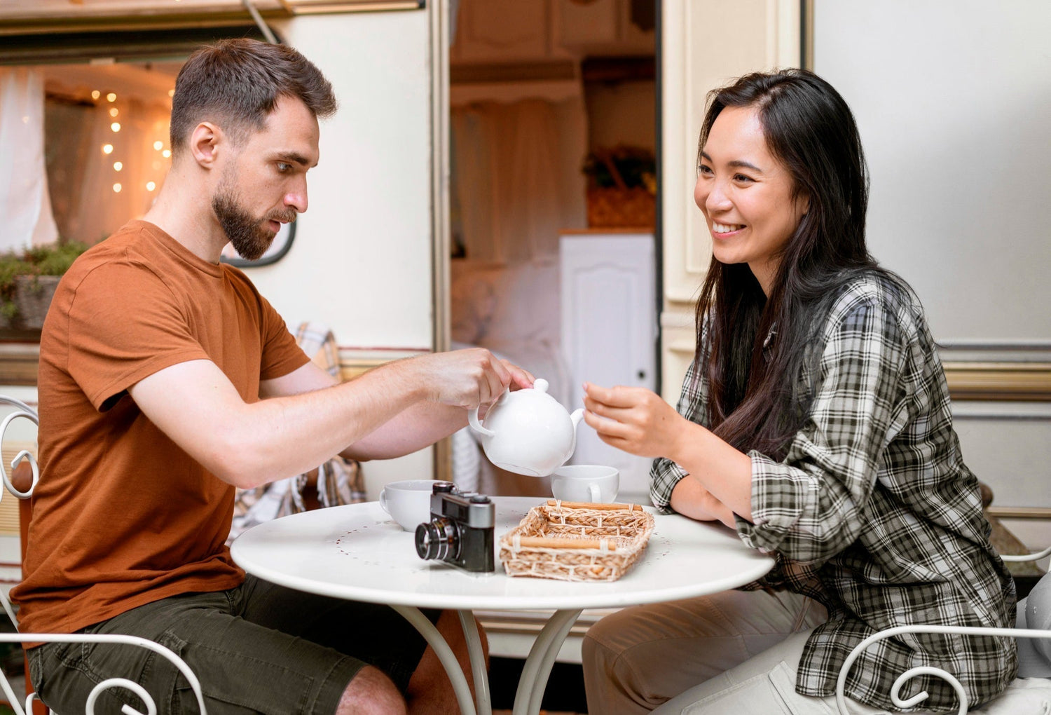 Two people laughing at a cafe table, warm window light, relaxed posture, coffee cups between them