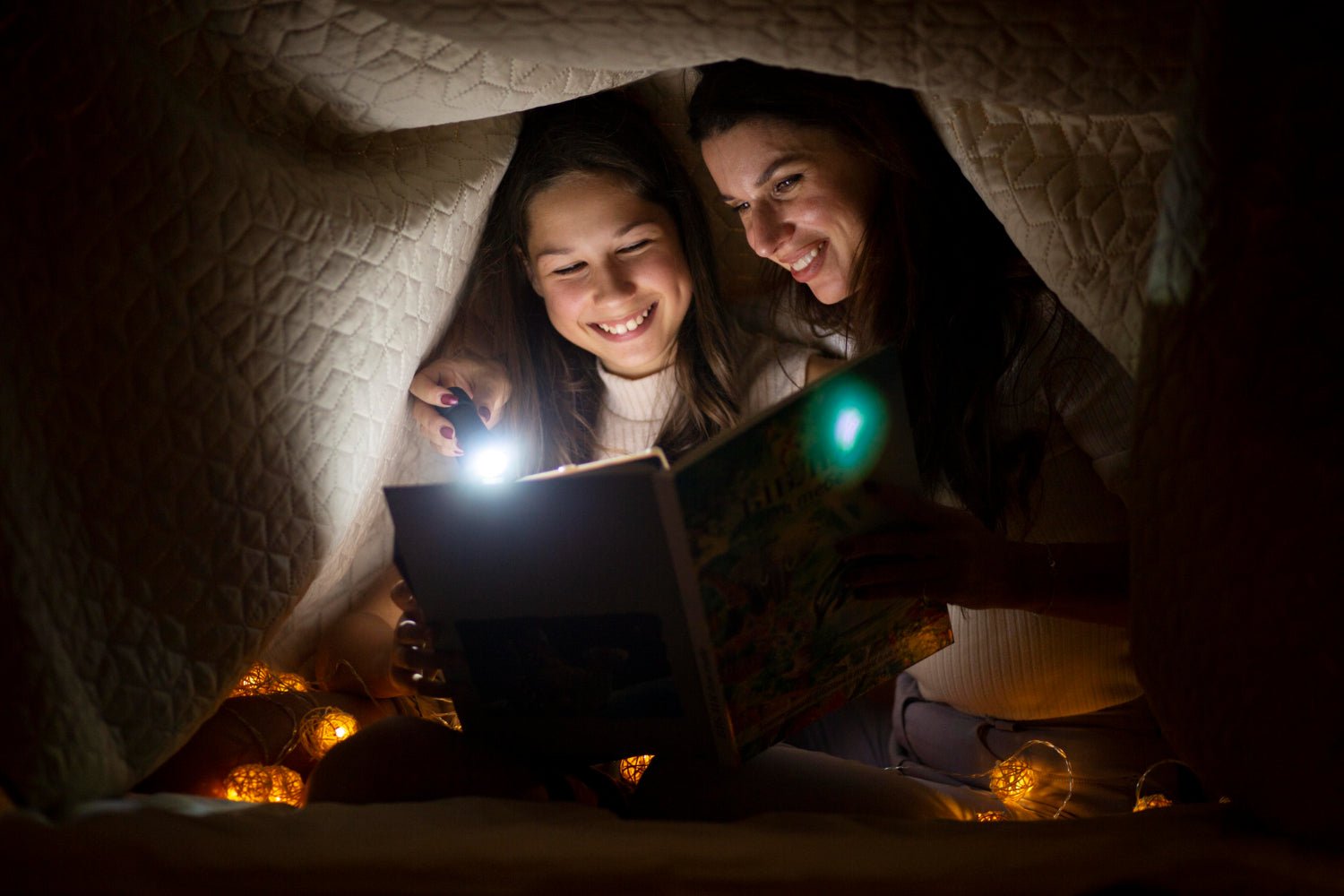 friends in pajamas building a blanket fort with string lights and sleeping bags spread out