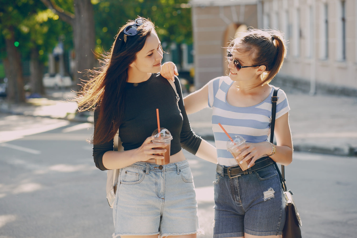 two friends laughing on a sidewalk as one adjusts the other’s backpack