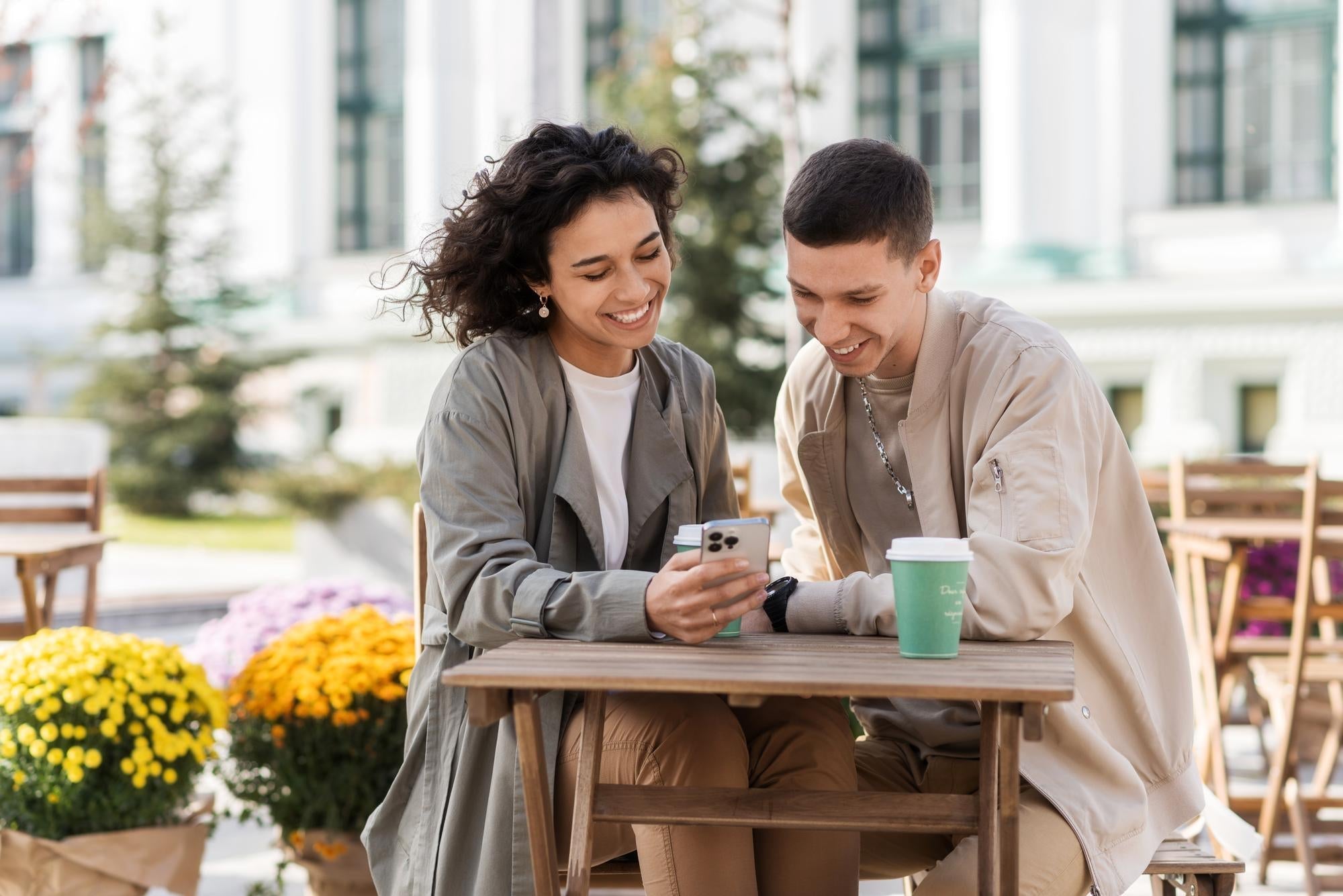 Two people laughing at an outdoor cafe, warm light, relaxed posture