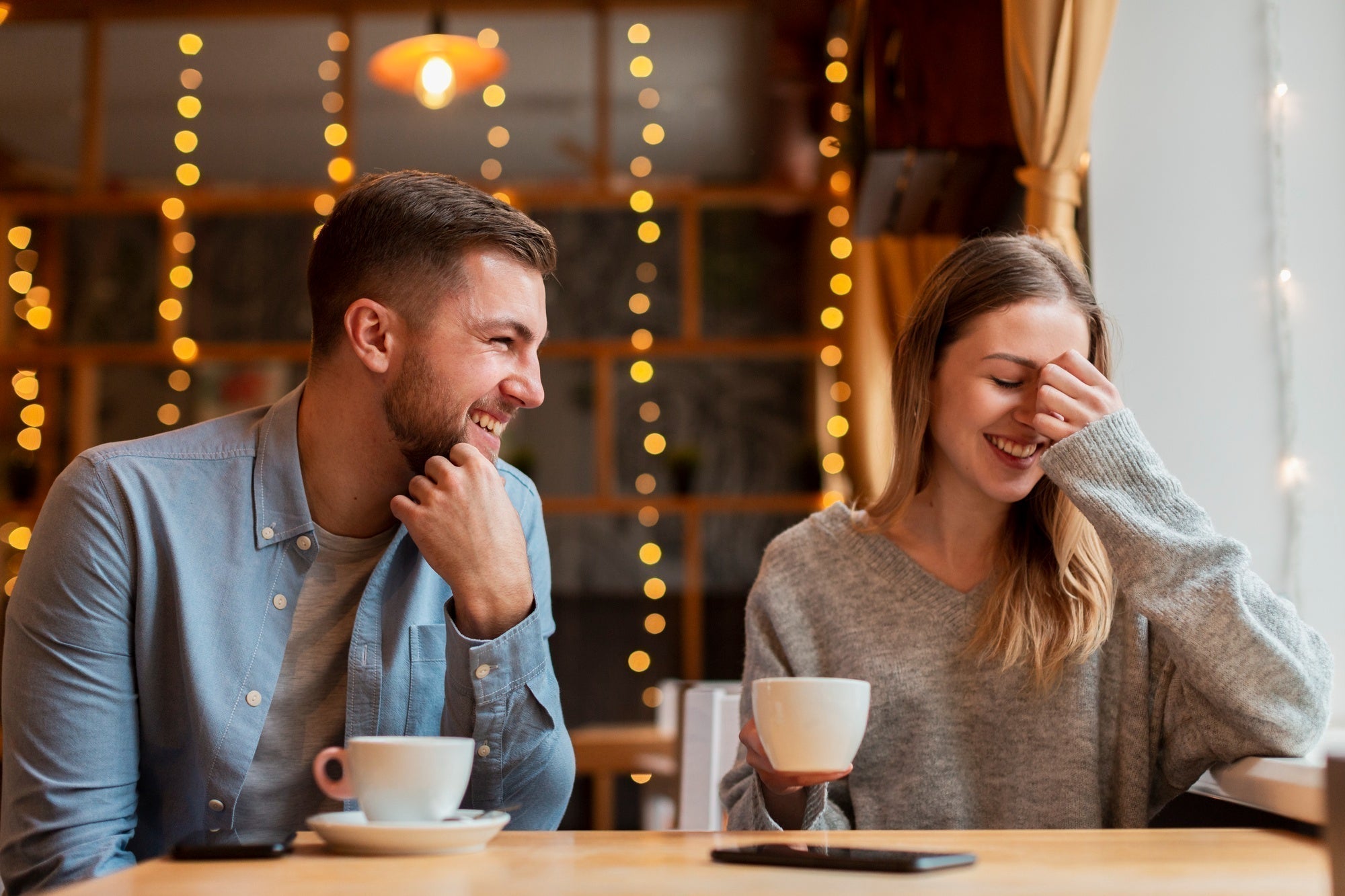 Two people smiling at a cafe table, relaxed posture, soft window light