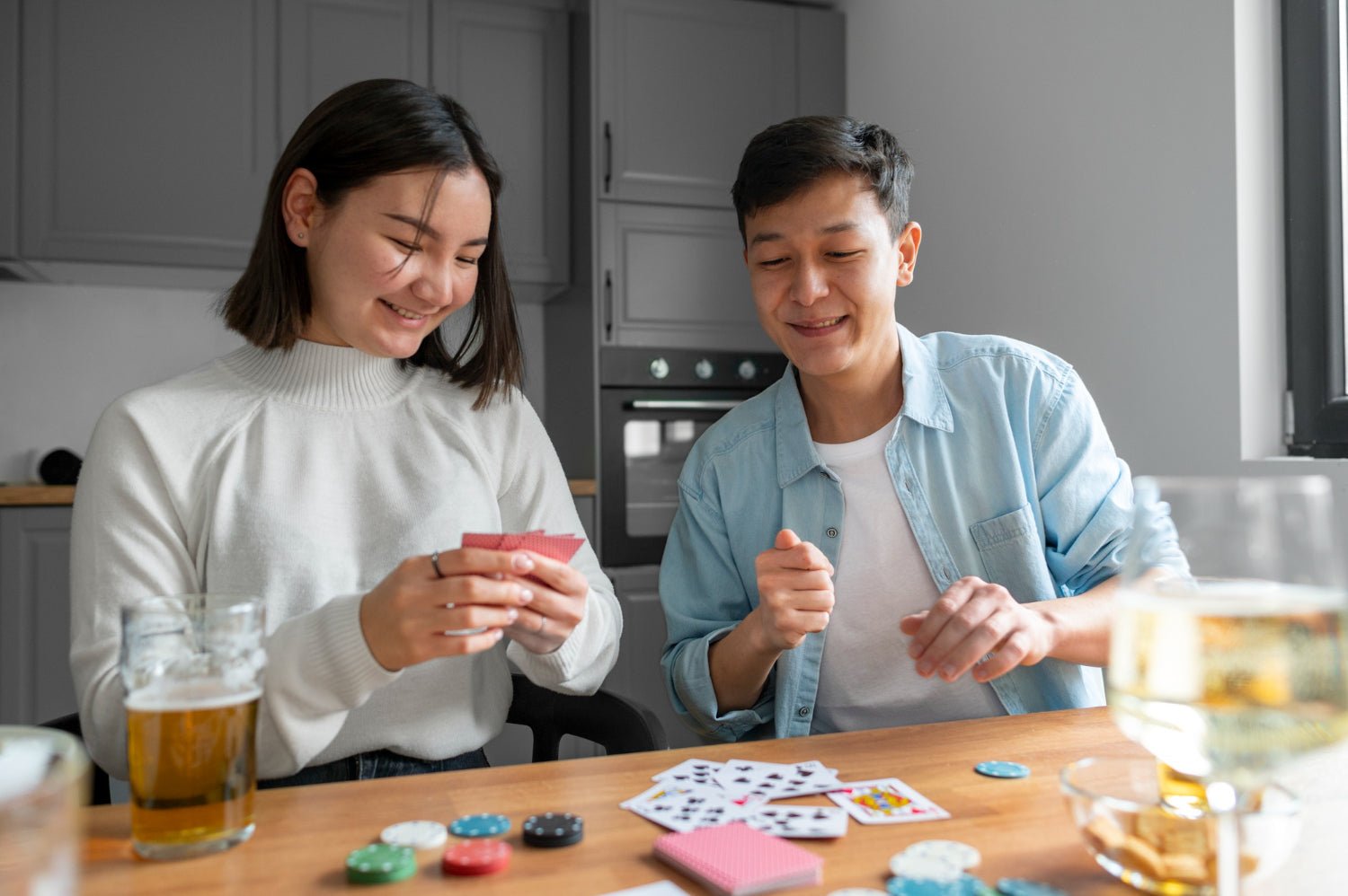 , two adult siblings laughing at a kitchen island filled with snacks and a deck of cards